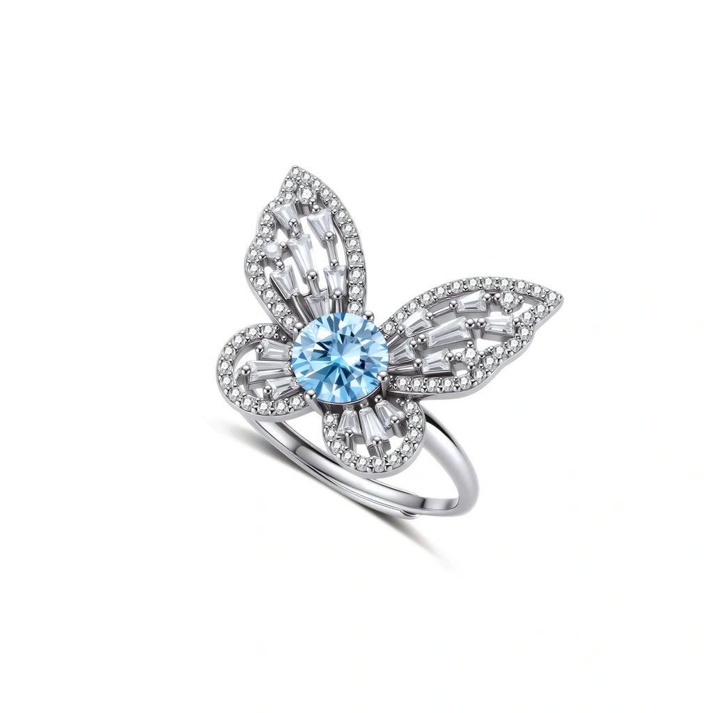 Sterling silver ring with blue moissanite center stone surrounded by clear stones in butterfly wing pattern on white background