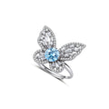 Sterling silver ring with blue moissanite center stone surrounded by clear stones in butterfly wing pattern on white background