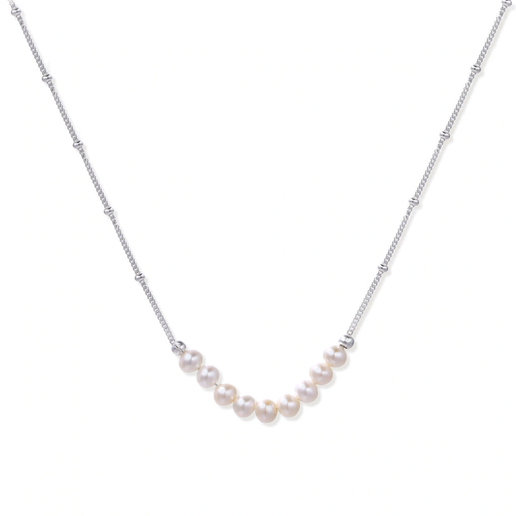 Delicate sterling silver chain necklace with small freshwater pearls arranged in a curved smile arc on cream background.