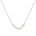Delicate sterling silver chain necklace with small freshwater pearls arranged in a curved smile arc on cream background.