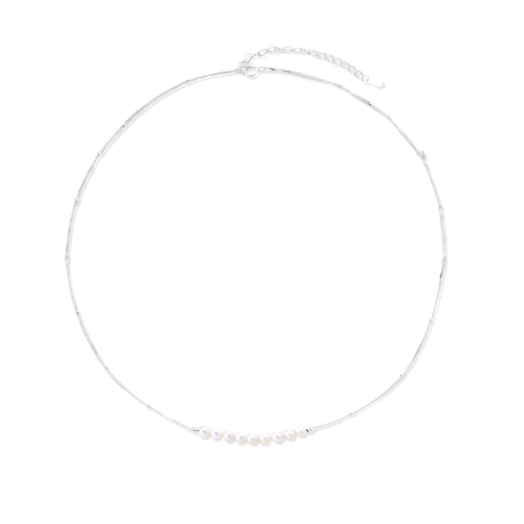 Delicate sterling silver chain necklace with small freshwater pearls arranged in a curved smile arc on cream background.