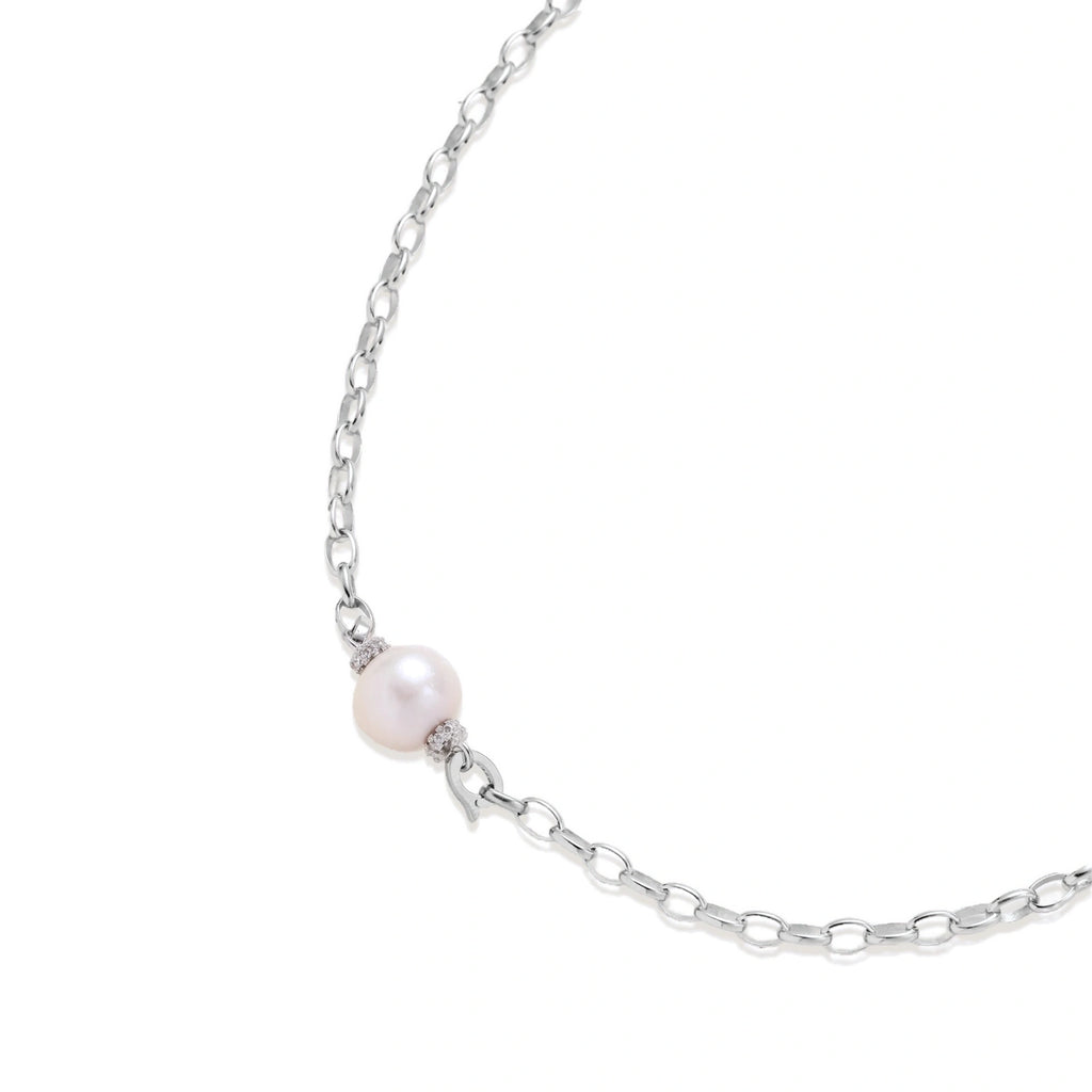 Dainty rhodium-plated silver chain necklace with centered 10mm freshwater pearl and crystal accents on cream background