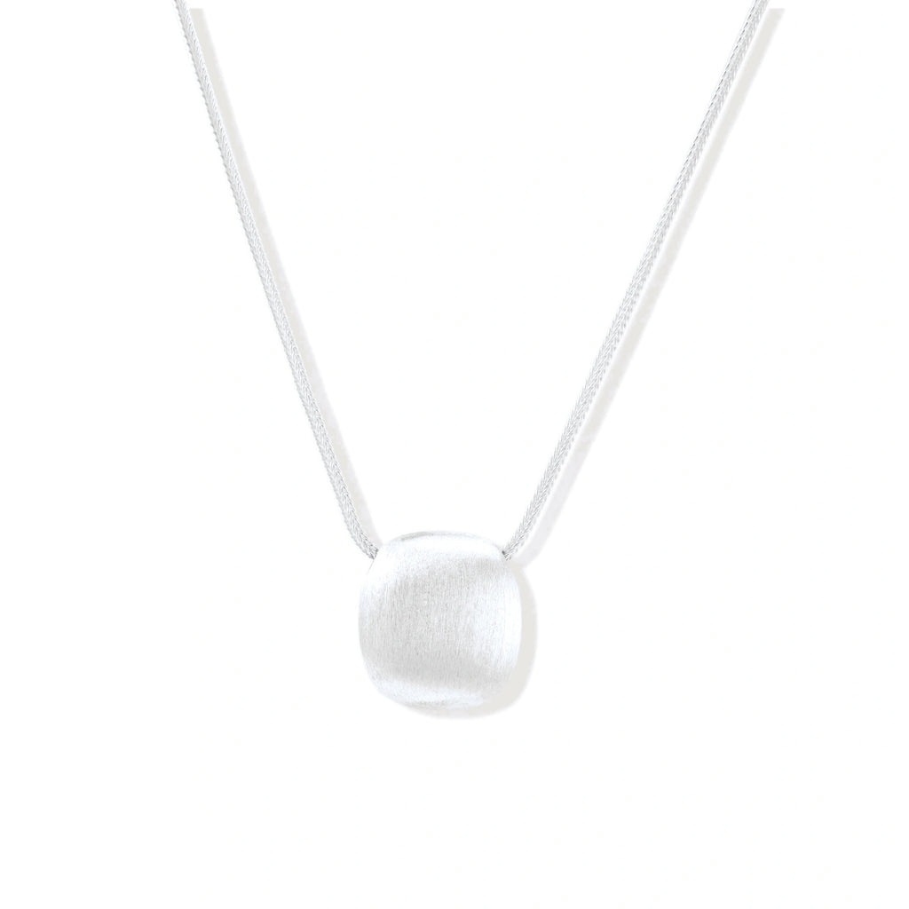 Minimalist brushed sterling silver dome pendant on delicate chain against cream background, showing matte textured finish