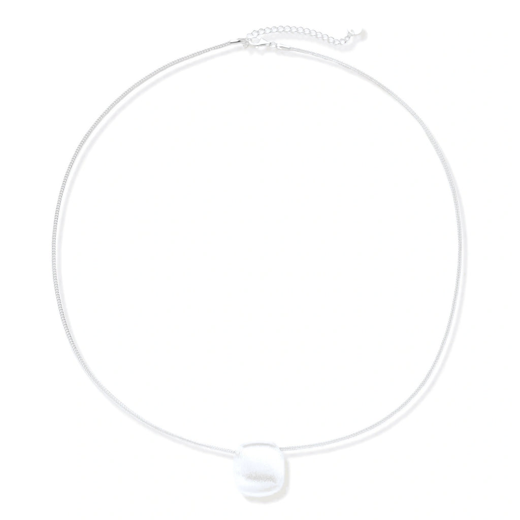 Minimalist brushed sterling silver dome pendant on delicate chain against cream background, showing matte textured finish