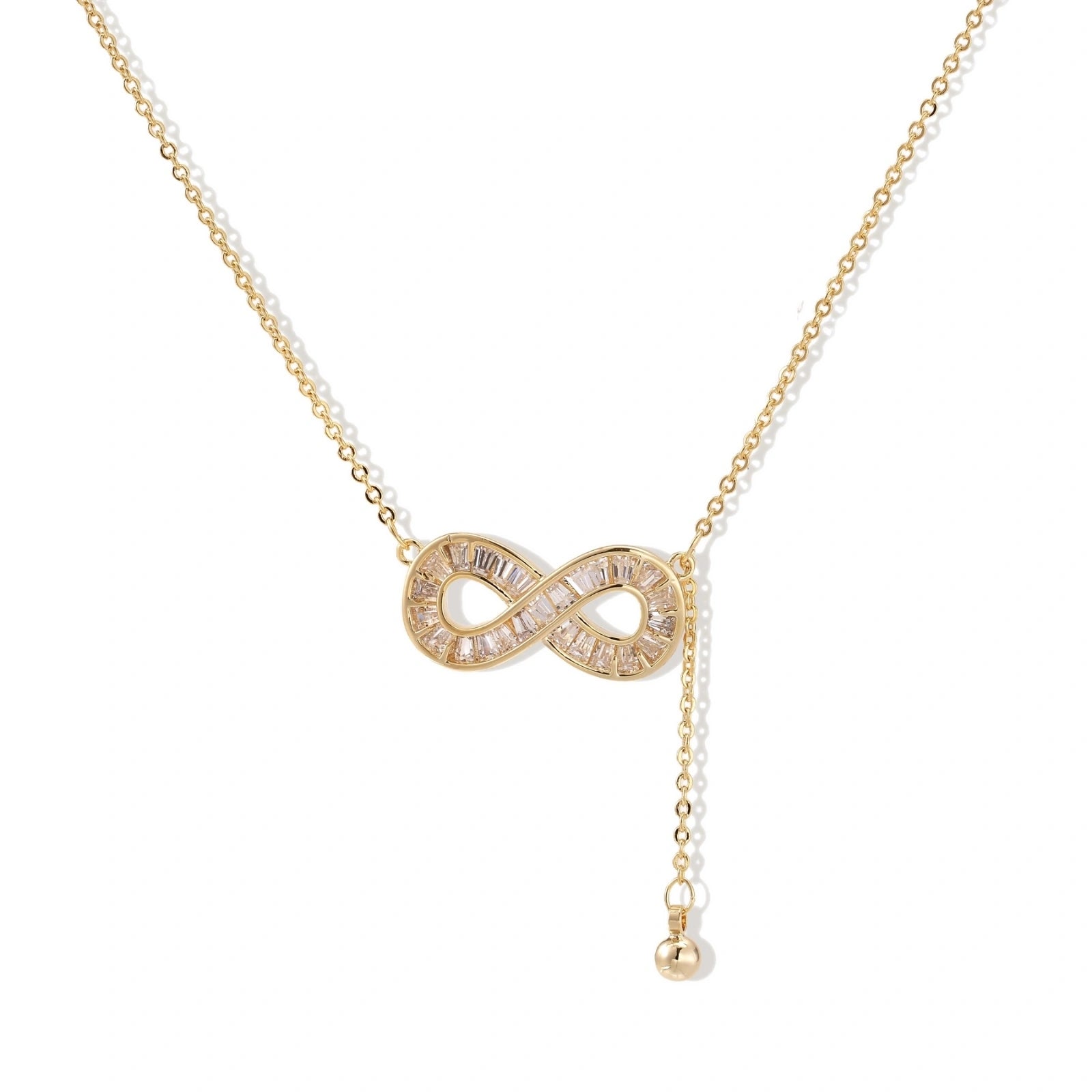 Gold infinity pendant with baguette crystals on adjustable chain against cream background.